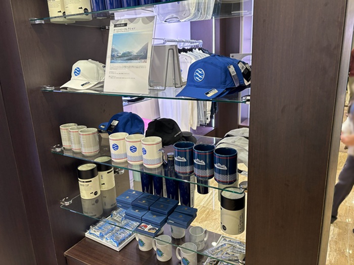 三井オーシャンフジ ロゴ入りキャップやマグカップみなど、限定グッズが並ぶオーシャンブティックの棚
