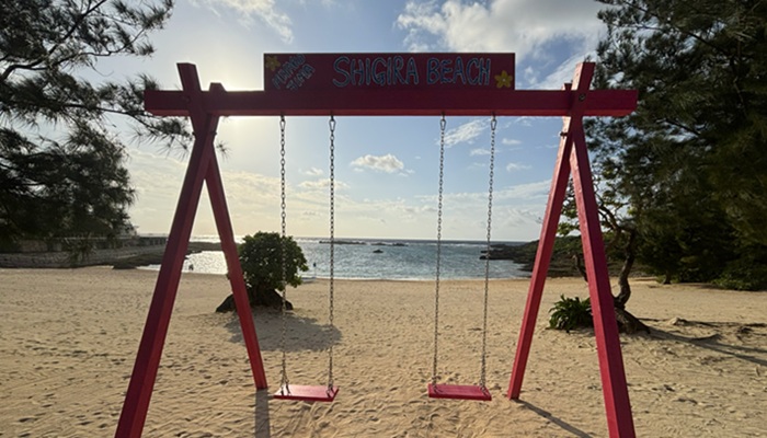 シギラビーチに設置されたピンク色の木製ブランコ。砂浜に映る影と海を望むフォトスポット