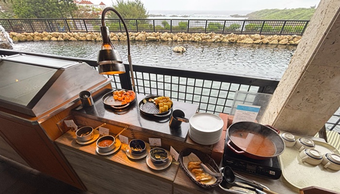 シギラミラージュ「タートルベイ」のライブキッチン。ブイヤベースなど温かい料理が並び、背景に海と噴水が広がる