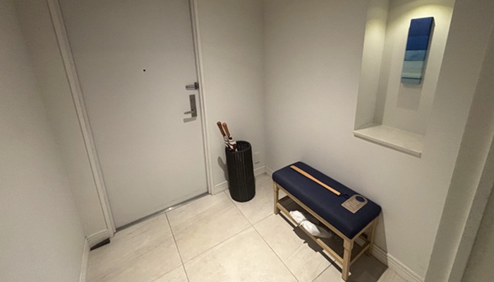 シギラミラージュ プールヴィラプレミアの玄関。腰掛け用ベンチ、傘立て、壁のニッチに飾られた青いアートがある広々とした空間